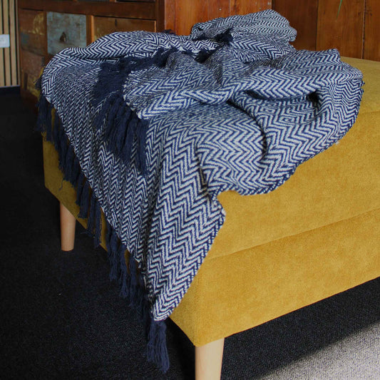 Blue patterned throw blanket with tassels draped over a yellow couch.